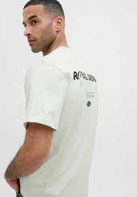 Lichtgrijze katoenen T-shirt met korte mouwen, voorzien van een zwart tekstontwerp op de achterkant en een cirkelvormig grafisch detail. Soepele textuur.