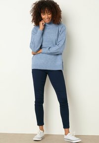 Pullover a maglia azzurro chiaro con collo alto, polsini a coste e spacco laterale, abbinato a jeans skinny in denim scuro e sneakers bianche.