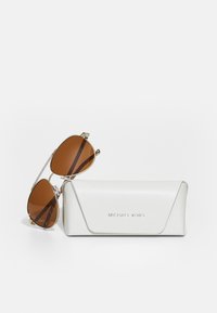 Brune solbriller med gultone metalramme, som leveres med et tekstureret hvidt etui prægede med "MICHAEL KORS."