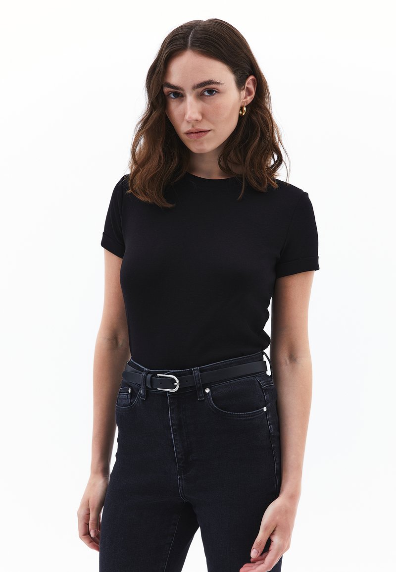 Černé bavlněné tričko s krátkým rukávem, přiléhavý střih a kulatý výstřih. V kombinaci s černými džínami s vysokým pasem a černým opaskem.