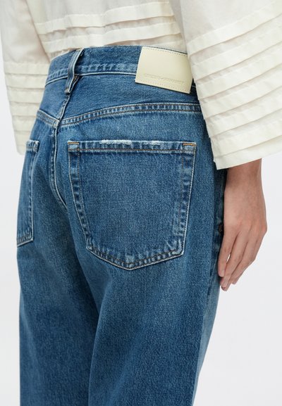 Svetlomodré denimové džínsy s priamym strihom nohavíc, s vreckami vzadu a krémovou nálepkou na páse pre branding.