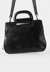 Musta nahkainen käsilaukku, jossa on sileä pinta, suorakulmainen muoto, lyhyt kahva ja säädettävä hihna. Varustettu metallisella soljella.