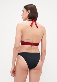 To-delt bikini med rød halterneck-top med en sløyfe og svart bunn. Glatt stoff og minimalistisk design med sideakenter.