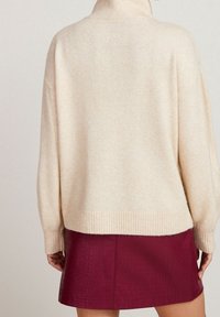 Pull en maille couleur crème avec un col montant, des poignets et un ourlet côtelés, associé à une mini-jupe en similicuir bordeaux à motif crocodile.