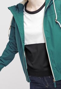 Letvæg teal jakke med en hvid og sort farveblok sweatshirt under. Har en snoretræk hætte og lynlås lukning.
