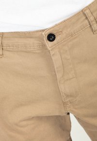 Beige cotton chinos featuring a button closure, standard waistband, and subtle stitching details. Smooth texture with a tailored fit.