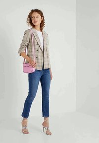 Blazer à carreaux à double boutonnage de couleur beige clair avec des rayures foncées, associé à une chemise blanche, un jean bleu, des sandales à talons argentées et un sac bandoulière rose.