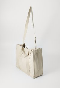Borsa tote in tela beige con due manici corti e una lunga tracolla regolabile, caratterizzata da una forma rettangolare e cuciture robuste.