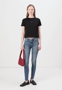 Tricou scurt negru cu un logo mic, blugi albaștri ajustați, mocasini negri și o geantă roșie de umăr. Design simplu, aspect casual.