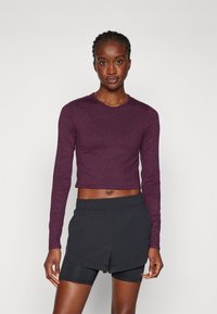 Maroon cropped long-sleeve top with a round neckline, paired with black athletic shorts. The outfit features a smooth, soft texture.