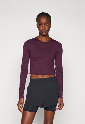 Maroon cropped long-sleeve top with a round neckline, paired with black athletic shorts. The outfit features a smooth, soft texture.