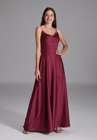 Robe de soirée en satin bourgogne avec un décolleté cowl, des bretelles spaghetti, et une jupe fluide, dotée d'une fente sur le côté et d'un ourlet au niveau des chevilles.
