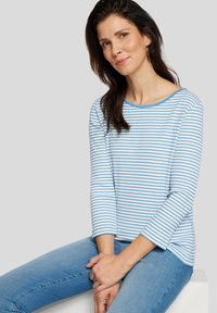 Blau-weiß gestreiftes Langarmshirt mit weitem Ausschnitt und gerippter Textur, kombiniert mit hellblauen Jeans. Glatte Stoffoberfläche.