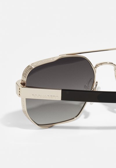Ochelari de soare aviator cu ramă metalică aurie, dotate cu lentile gri degradé. Au un sprijin frontal texturat și accente îndrăznețe pe brațele negre. Numele brandului este evidențiat.
