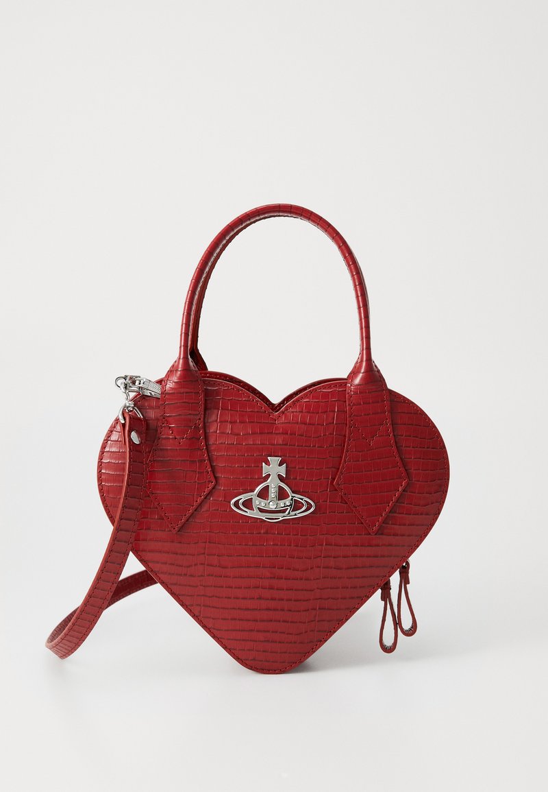 Czerwona torebka w kształcie serca z teksturą krokodyla, podwójnymi uchwytami, odczepianym paskiem i srebrnym emblematem w kształcie kuli z przodu.
