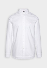 Camisa blanca de manga larga hecha de algodón texturizado, con un cuello abotonado, cierre frontal con botones y un pequeño logo en el pecho.