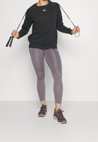 Czarny sweter z okrągłym dekoltem, fioletowe legginsy i ciemne sneakersy. Legginsy mają gładką strukturę i logo na dolnej części nogawki.