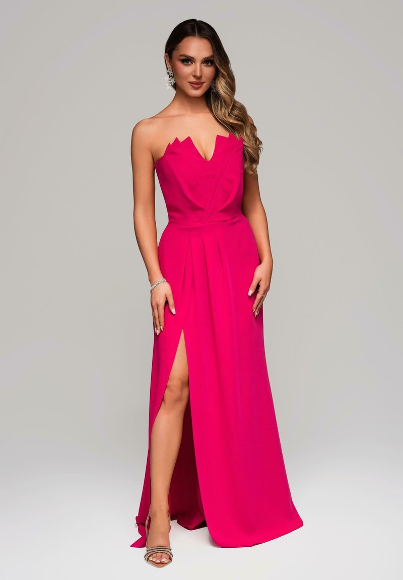 Abito lungo fucsia, con scollatura profonda e design del corpetto angolato. Presenta un'alta spacco e tessuto fluente. Accessori argentati in vista.