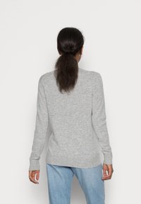 Grauer Pullover mit langen Ärmeln und rundem Halsausschnitt, aus weichem Material mit glatter Textur. Trägt dazu eine hellblaue Jeans.