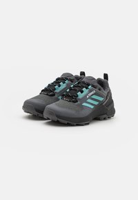Zapatillas deportivas grises con detalles en verde azulado, de tela de malla y suelas de goma. Presentan cordones negros y una tira en el talón para facilitar su uso.