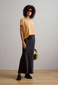 Oranžový top s krátkým rukávem, černá přiléhavá sukně, černé boty a zelená taška. Hladká tkanina, ležérní design, s uvolněnou siluetou.