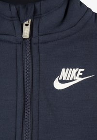Jachetă bleumarin cu fermoar, din material mix de bumbac, cu guler înalt, fermoar frontal și logo Nike brodat alb pe piept.