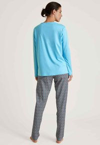 Lichtblauw langarmshirt gecombineerd met gestreepte pyjamabroek met geometrische vormen in blauw, grijs en witte tinten. Zachte stofstructuur.