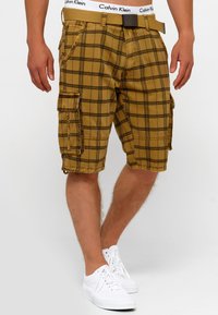 Kaki rutiga cargoshorts med flera fickor, dragsko i fållkanten och en blandning av bomullstyg. Bärs med vita sneakers och ett synligt bälte.