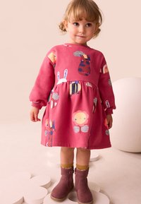 Lyserød jersey-kjole med legesyge dyre- og blomsterprint, lange ærmer og en rynket talje, kombineret med brune knæhøje støvler.