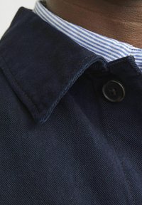 Navy jacket featuring a structured collar, button detail, and a striped fabric lining. The material appears textured and durable.