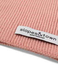 Tessuto rosa a righe con una morbida texture, dotato di un'etichetta bianca che recita "slopes&town AMSTERDAM." L'etichetta è cucita su un lato.