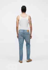 Λευκό αμάνικο, ανοιχτό μπλε τζιν με πίσω τσέπες, καφέ παπούτσια, υφή υλικού και ορατές ραφές στα τζιν.