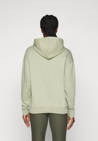 Felpa verde chiaro con un ampio cappuccio, vestibilità rilassata, polsini e orlo a costine, abbinata a leggings verde scuro. Tessuto di superficie liscia.