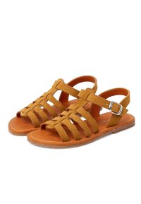 Sandales en suede marron avec des brides entrecroisées et une boucle réglable. Semelle plate avec des détails de couture sur les bords. Design à bout ouvert.