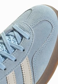 Gaiši zils zamšādas sneakers ar baltām sakraujamām svītrām, mīksti izlādēta potīte un auduma auklas. Iezīmēts ar teksturētu gumijas zoli, kas nodrošina saķeri.