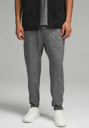 Grau Jogginghosen mit einem strukturierten, melierten Muster, mit einer schmalen Passform, elastischem Bund und kombiniert mit weißen Sportschuhen.