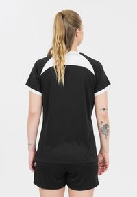 Svart idrottströja med vita detaljer, korta ärmar och rund halsringning. Slät tyg, avslappnad passform, tillsammans med matchande svarta shorts.