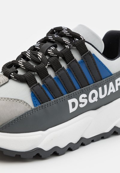Sneaker grigio e blu con materiale testurizzato, dotato di lacci neri, suola in gomma e logo bianco sul lato. Forma piatta e rotonda.