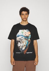 Sort kortærmet t-shirt med et grafisk design, der har et stiliseret ansigt og farverige accenter. Teksten nederst lyder "glemte ansigtstræk."