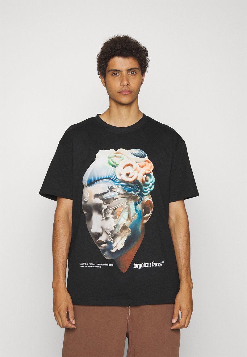 Sort kortærmet t-shirt med et grafisk design, der har et stiliseret ansigt og farverige accenter. Teksten nederst lyder "glemte ansigtstræk."