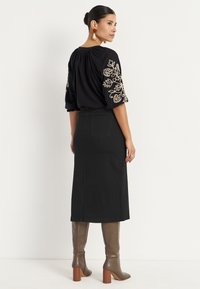 Zwarte blouse met bloemenborduursel op de mouwen, gecombineerd met een zwarte denim midi-rok. Draagt kniehoge bruin leren laarzen met hak.