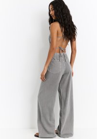 Grauer Denim-Overall mit tailliertem Oberteil und weitem Beinschnitt, ausgestattet mit einem Bindeband-Design, weicher Textur und Gesäßtaschen.