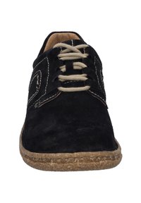 Chaussure en daim noir avec des lacets beiges, bout rond et semelle texturée ressemblant à du liège naturel, agrémentée de coutures contrastées.