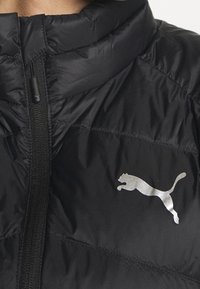 Czarna kurtka puchowa z wysokim kołnierzem, zapięciem na zamek błyskawiczny oraz odblaskowym, srebrnym logo Pumy po lewej stronie klatki piersiowej. Gładka, błyszcząca tekstura.