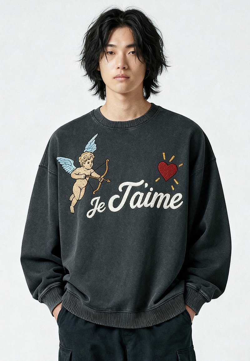 Jeune personne aux cheveux noirs mi-longs portant un sweat-shirt noir orné d'un chérubin avec un arc et des flèches, un cœur rouge et le texte "Je T’aime".