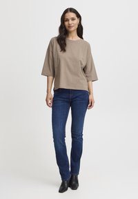 Lysbrun cropped t-shirt med brede ærmer, parret med mørkeblå lige bukser og sorte ankelstøvler. Enkel, afslappet design.