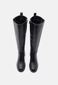 Térd magas fekete bőr csizmák oldalsó cipzárokkal, lapos talppal és sima felülettel. A tetején húzófülek találhatók a könnyű felvétel érdekében.