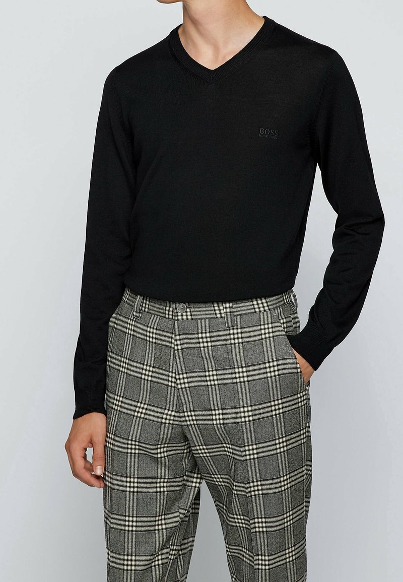 Svart v-ringad tröja i ett slätt stickat tyg, kombinerad med grå rutiga byxor med vita och svarta rutor, i en slim fit-design.