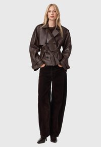 Bruine leren dubbelzijdige jas met een riem in de taille, brede puntkraag en lange mouwen. Gecombineerd met donkerbruine wijde broek.