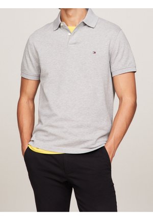 Polo shirt in cotone grigio con colletto a bavero, maniche corte e un piccolo logo sul petto. Abbinato a pantaloni neri e una maglietta gialla sotto.